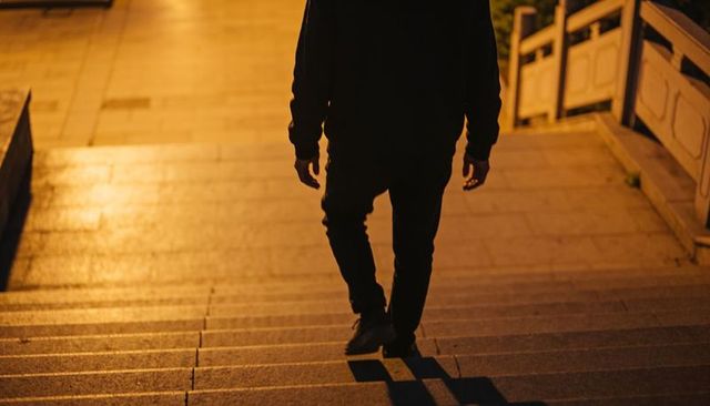 Man descending stone steps at night casting long amber shadows moody urban silhouette