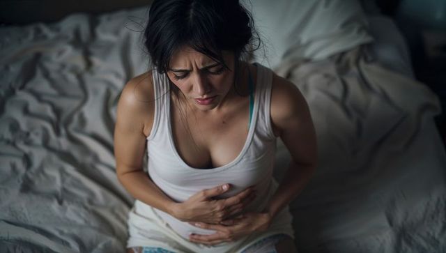 Woman sitting on bed with hands on stomach in solitary contemplation
