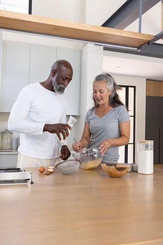 Middle-aged couple preparing batter together on sunlit modern kitchen island