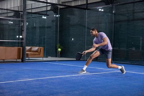 African american athlete lunging to return neon ball on indoor padel court