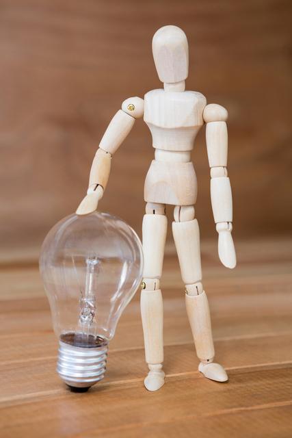 Wooden figurine standing with a light bulb on a wooden surface. This image can be used to represent creativity, innovation, and new ideas. It is suitable for use in articles, presentations, and marketing materials related to design, art, and inspiration.