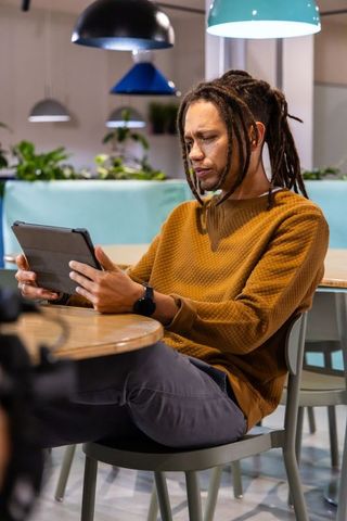 African American Man Working on Tablet in Modern Coworking Cafe with Dreadlocks