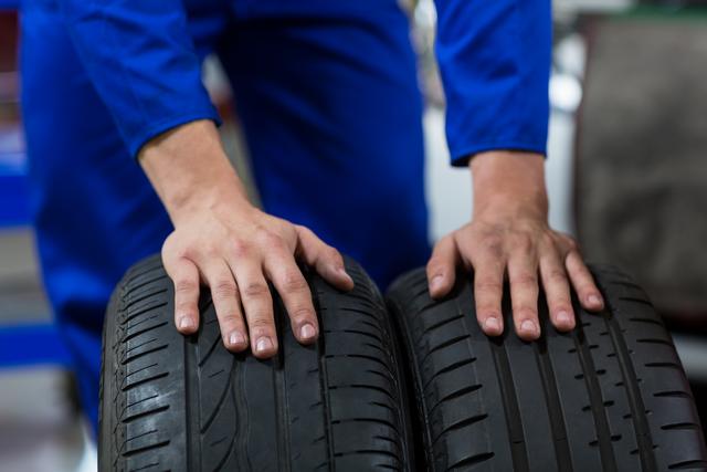 Mechanic's hands inspecting car tires in an auto repair shop. Useful for illustrating automotive maintenance, vehicle service, and repair shop services. Ideal for websites, brochures, and advertisements related to car repair, tire services, and automotive workshops.