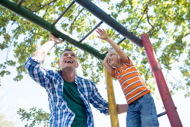 Father and son bonding while playing on a jungle gym at a playground. Ideal for use in family-oriented advertisements, parenting blogs, and outdoor activity promotions. Highlights themes of family fun, outdoor play, and parent-child relationships.
