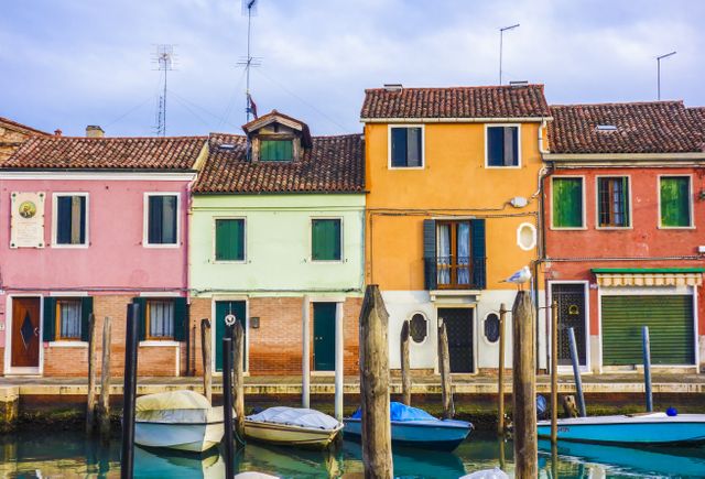 Colorful houses reflecting in a serene Venetian canal, showcasing traditional architecture and vibrant pastel colors. The boats docked along the canal add charm and capture the tranquil atmosphere of Italian city life. Perfect for promoting travel destinations, European tourism, and cultural heritage tours.