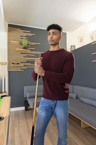 Young man holding pool cue in modern lounge wearing maroon sweater and jeans casual