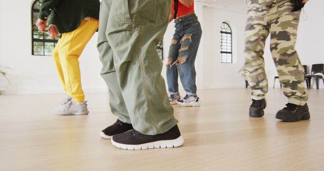 Four dancers are practicing a hip-hop dance routine in a brightly lit dance studio. The dancers wear casual, loose-fitting clothes and sneakers suitable for dance movements. This image is suitable for topics on dance workshops, practicing choreography, urban culture, and active community events.