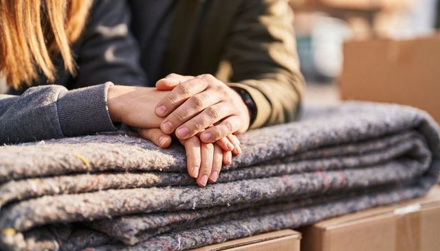 Resting overlapped hands on folded moving blankets conveying warmth and support