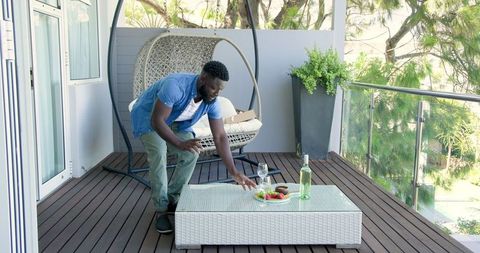 Man Preparing Snacks and Wine on Modern Balcony with Swing Chair