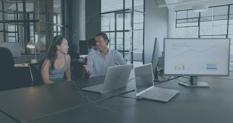 Young professionals collaborating at modern coworking table with laptops and analytics monitor