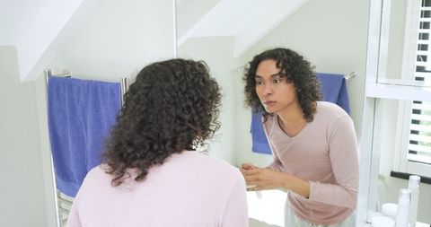 Nonbinary person practicing morning skincare at bathroom sink facing mirror with daylight