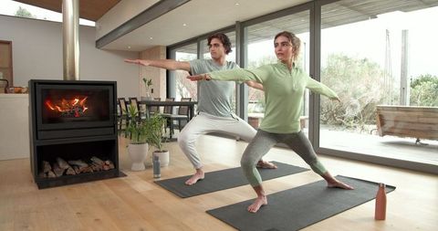 Couple Practicing Yoga in Stylish Modern Living Room with Fireplace