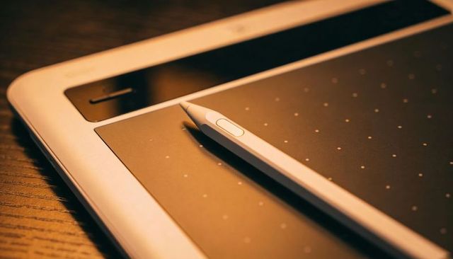 Resting stylus on dotted drawing tablet with silver bezel, wood desk, warm ambient light