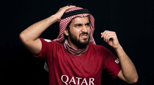 Frustrated middle eastern football fan wearing qatar jersey and red keffiyeh clutching head