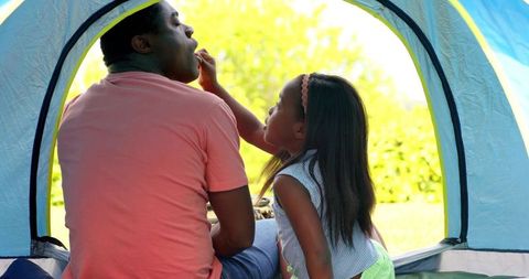 Father and daughter bonding inside a tent on sunny day