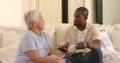 Senior woman and African American man discussing letter on sofa, caregiving conversation