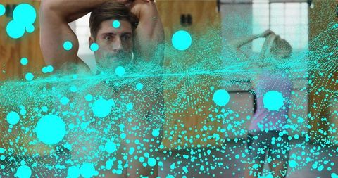Shirtless man stretching arms in gym with teal particle overlay, woman stretching behind