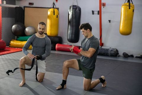 Kneeling mma partners wrapping hands and warming up before sparring in modern fight gym