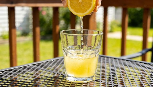 Hand squeezing lemon over glass on sunny patio creating refreshing citrus splash