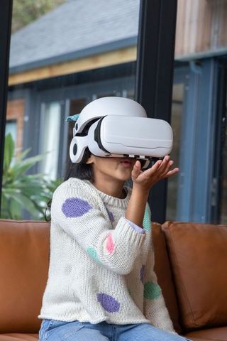 Child exploring virtual reality wearing white vr headset on brown leather couch at home