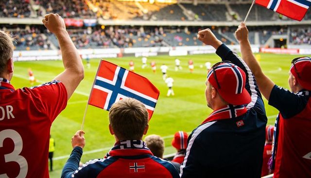 Norwegian football fans cheering and waving flags in stadium stands during outdoor match