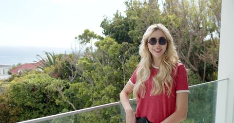 Young woman wearing red ringer tee and sunglasses on glass balcony with coastal view
