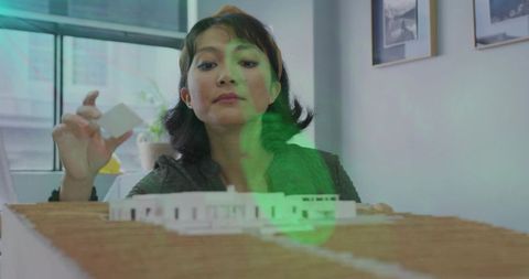 Asian architect placing foam block on modern architectural model in bright design studio