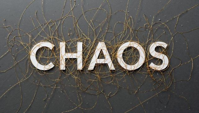 Chaos typography with gold thread tangle on dark slate flatlay