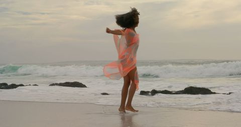 Energetic Young Woman Joyfully Dancing on Beach at Sunset