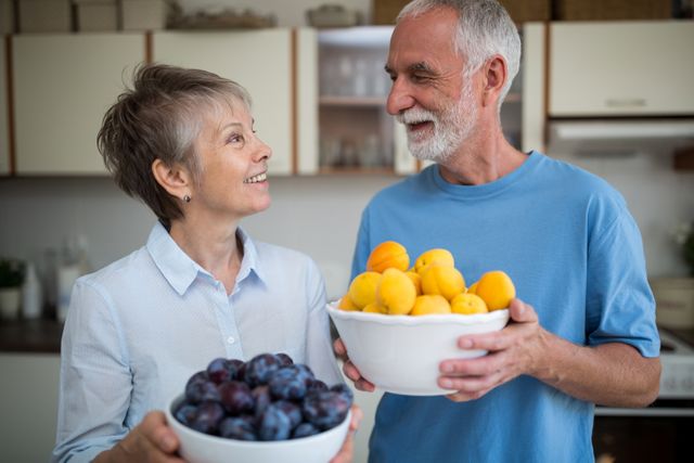 Senior couple holding bowl of apricot and grapes in kitchen