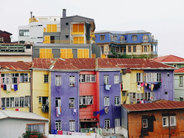 Vibrant multi-colored houses create a picturesque and vibrant urban neighborhood scene. The varied colors of the buildings, including purple, yellow, and red, add charm and personality to the architecture. This image is perfect for use in travel and tourism promotions, urban development articles, or blog posts about unique worldwide architecture. It highlights the cultural and artistic expression through residential areas.