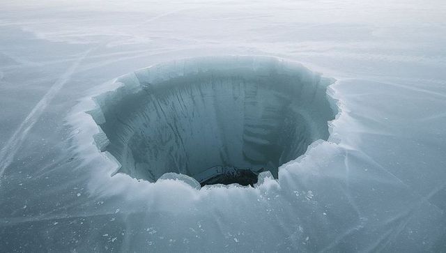 Scalloped ice abyss in frozen lake revealing deep circular glacial opening