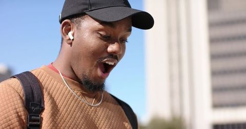 African american man reacting while listening with wireless earbuds in urban daylight