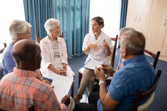 Female doctor engaging in a group discussion with senior citizens at a retirement home. Ideal for use in healthcare, elderly care, senior living, and community support materials. Can be used in brochures, websites, and articles focusing on medical consultation, wellness, and aging.