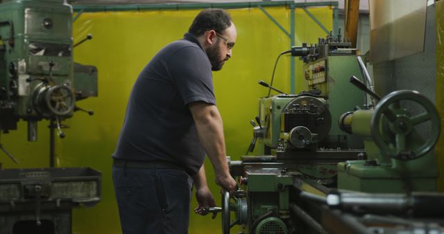 Illustrates a skilled male machinist operating machinery in a manufacturing workshop. Suitable for use in articles or advertisements related to industrial manufacturing, engineering, and vocational training.