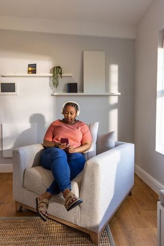 African american woman relaxing with headphones and smartphone in sunlit living room