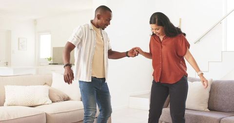 Young couple practicing balance steps and holding hands in bright modern living room