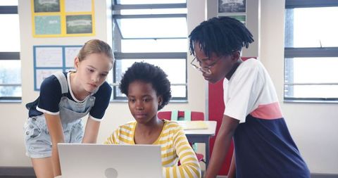 Diverse School Children Learning Together Around Laptop in Classroom