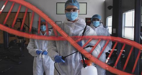 Sanitizing gym with ppe sprayers wearing protective suits and gloves with dna helix overlay