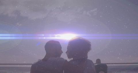 Silhouetted couple leaning close on waterfront bench at dreamy twilight with lens flare