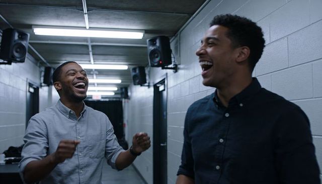 Laughing colleagues sharing animated chat backstage corridor with speakers and fluorescent lights