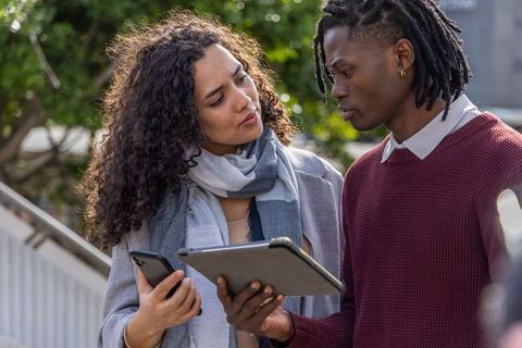 Diverse coworkers collaborating outdoors reviewing tablet and phone on urban stairs