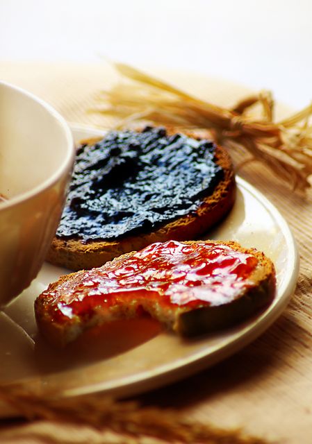 Close-up of two slices of toast spread with blueberry and strawberry jam. One slice has a bite taken out of it, creating a candid and inviting scene. This image is perfect for food blogs, breakfast menu design, healthy eating articles, and social media promotions related to breakfast ideas or homemade snacks.