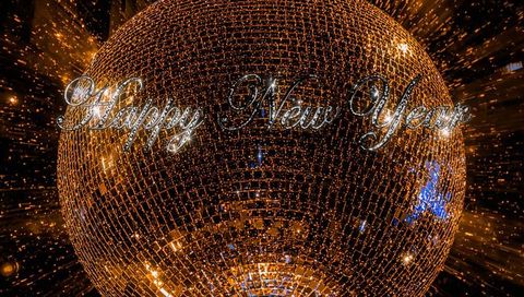 Golden mirrored disco ball with sparkling happy new year script and radiant light burst