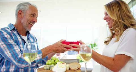 Joyful mature couple sharing surprise gift during light breakfast