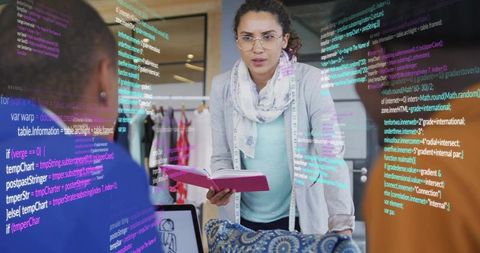 Designer Leaning Over Workbench Holding Notebook and Tape Measure Collaborating with Developers