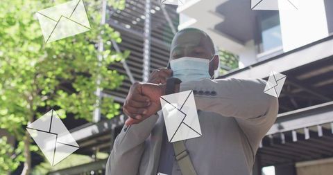 African american man checking smartwatch while talking on phone, masked urban professional