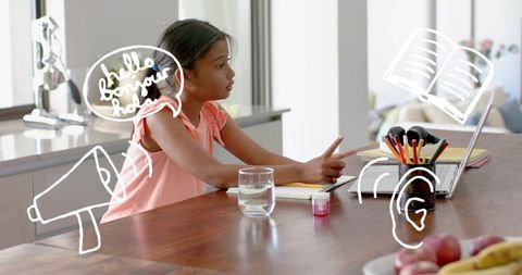 Young girl pointing at laptop while learning at kitchen table with playful doodles