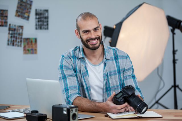 Male photographer in a studio smiling while reviewing photos on his digital camera. Ideal for articles or advertisements related to photography, creative professions, technology, and photo editing. It can also be used in educational materials for photography courses or promotional content for photography equipment.