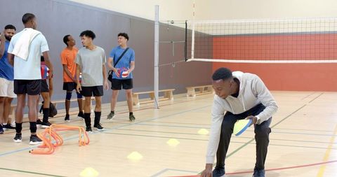 Setting up volleyball agility drill while multiracial teammates waiting on indoor court